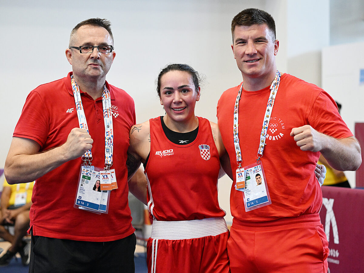Three individuals in red athletic attire pose with medals and lanyards, displaying a boxing stance indoors.
